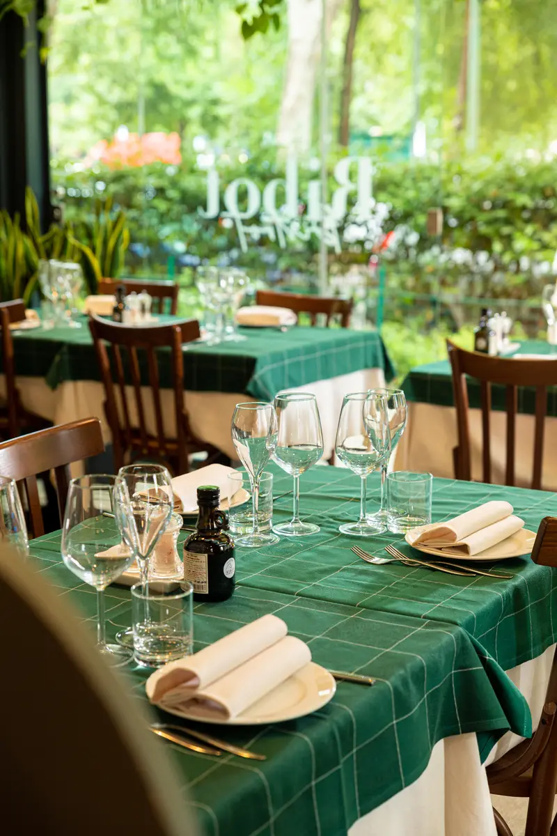 Le tovaglie verdi a quadri del Bistrot davanti alla vetrata col nome Ribot, e fuori il verde