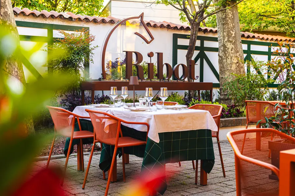 Il giardino nascosto del Borghetto: tavoli con le tovaglie bianche e verdi, sedie arancio, e sul muro l’insegna col cavallo di Ribot