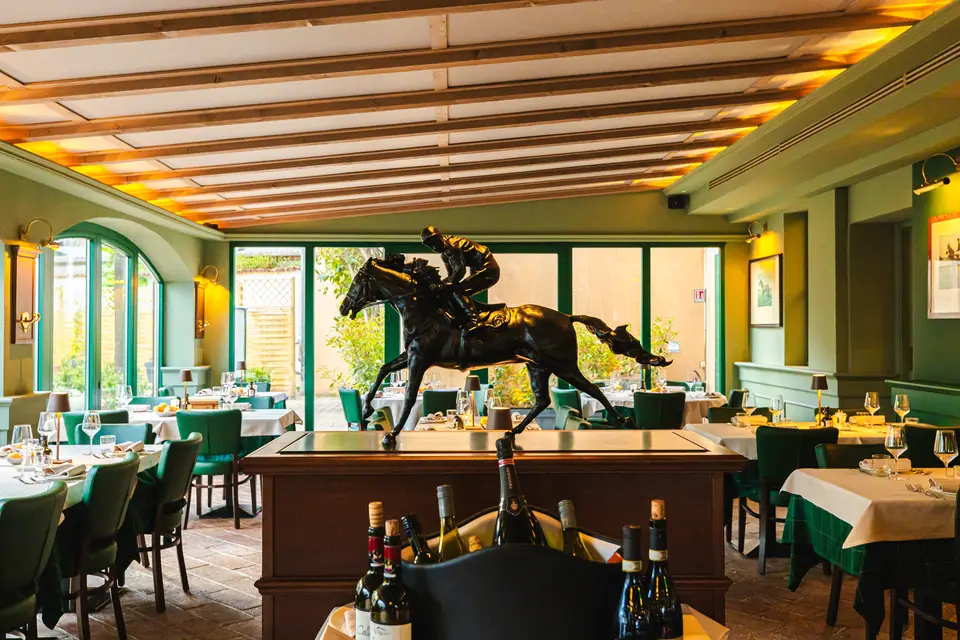 La sala del Borghetto apparecchiata: sedie di pelle verde, tovaglie bianche e verdi, e al centro il cavallo di bronzo col fantino