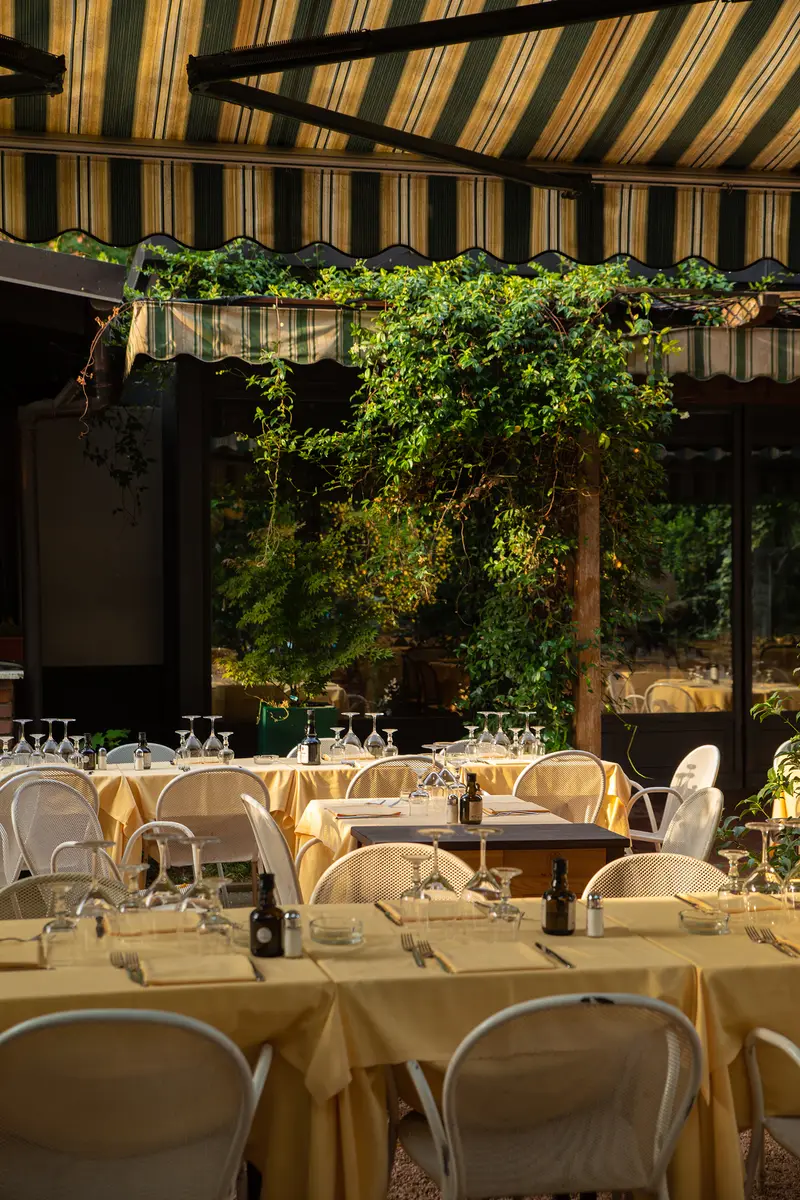 Il giardino di Ribot a San Siro sotto il tendone a righe verdi, coi tavoli apparecchiati di giallo fra le piante